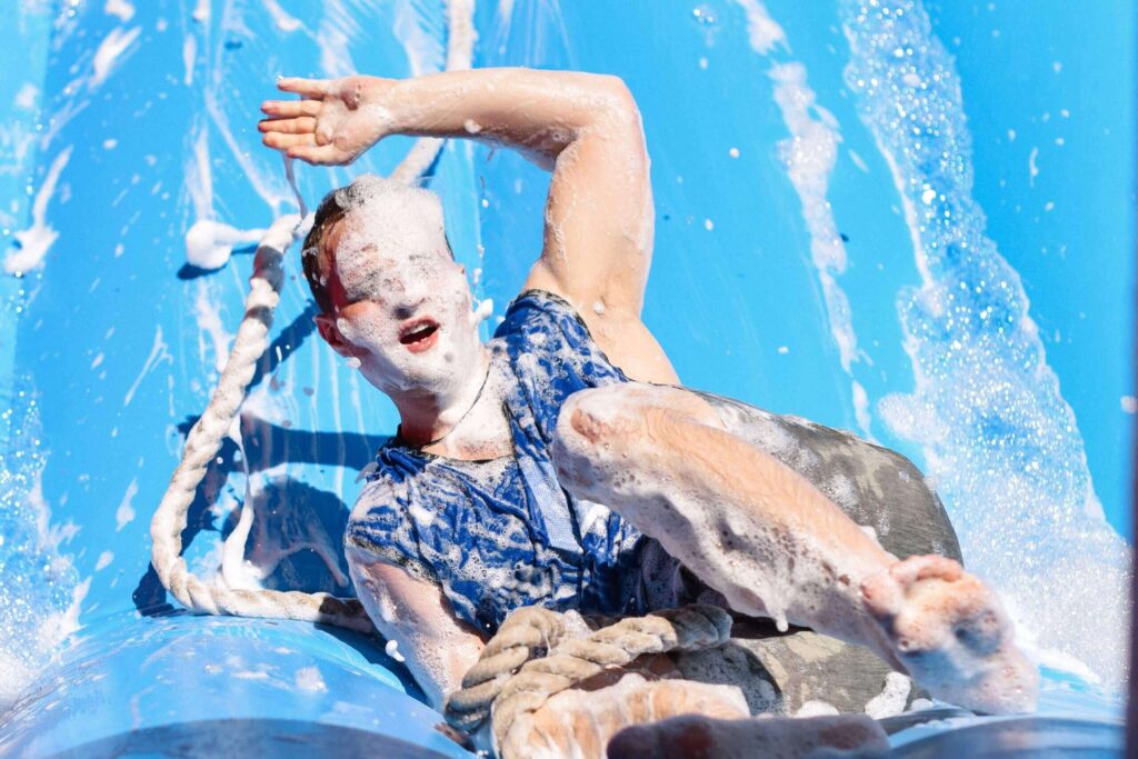 Participant enjoying It’s a KnockOut event, sliding down a foamy inflatable slide