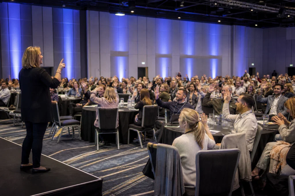 Facilitator leading a seated conference energiser in a large room