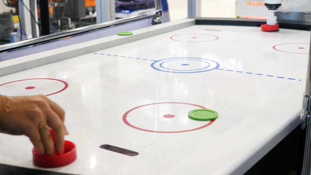 Air,Hockey,Table,And,Person's,Hand,Playing,With,White,Robot