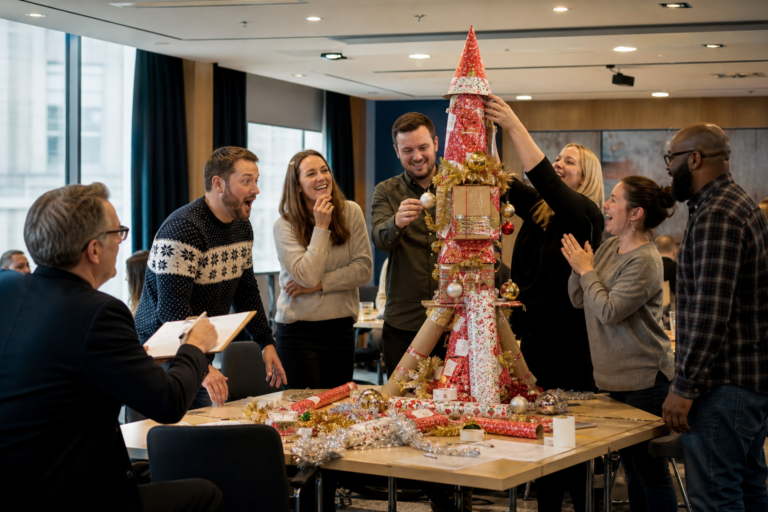 UK corporate team competing in a festive Taskfather challenge with a host judging Christmas task props in a meeting room