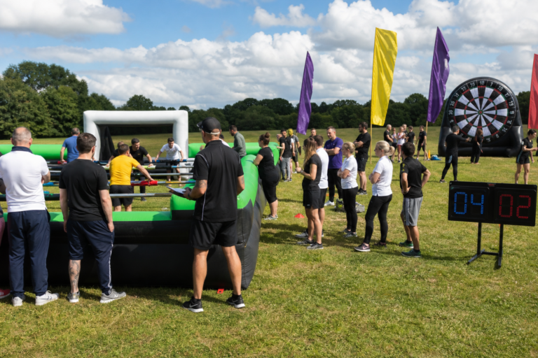 Wide shot of a UK corporate group taking part in the World Cup Fever football-themed team building event outdoors with inflatables and live scoring